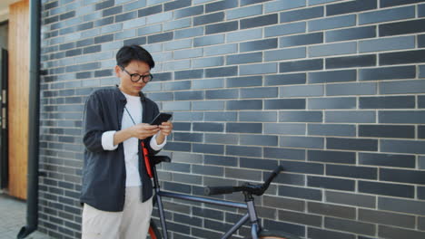 Asiatische-Frau-Steht-Mit-Dem-Fahrrad-Auf-Der-Straße-Und-Benutzt-Smartphone